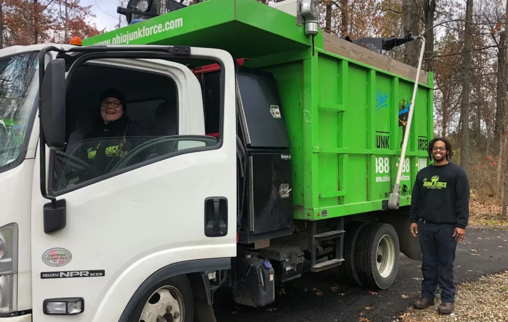 Ohio Junk Force team member standing next to a green and white junk removal truck while another crew member smiles from the driver’s seat.