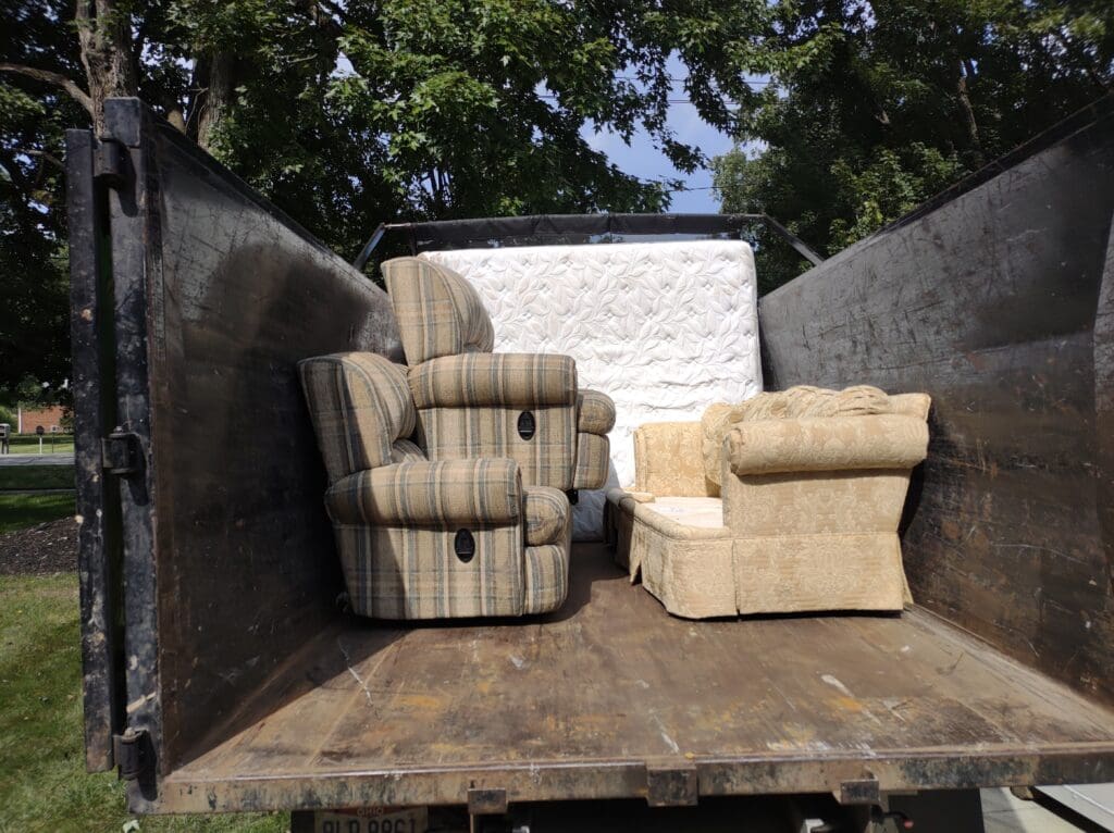 Usable unwanted furniture, including recliners, an upholstered chair, and a mattress, loaded neatly inside a junk removal truck for donation or disposal.