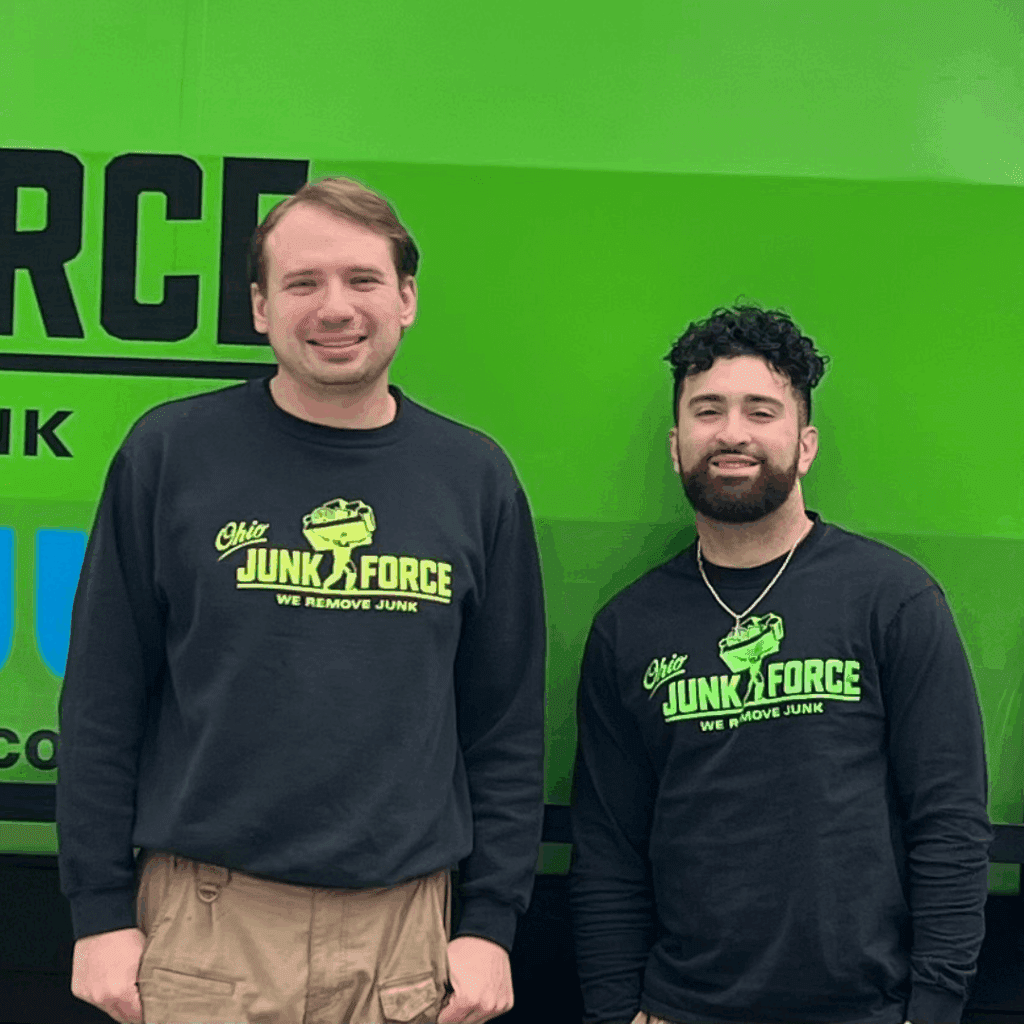 Two Ohio Junk Force team members in black branded shirts stand in front of a bright green company truck panel.