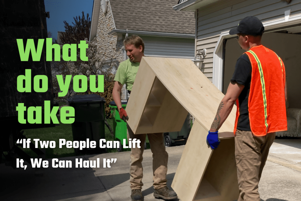 Two Ohio Junk Force workers—one in green shirt, the other in black shirt with orange vest—carry a tall wooden cabinet from house garage; green text reads "What do you take 'If two people can lift it. We can haul it.'"