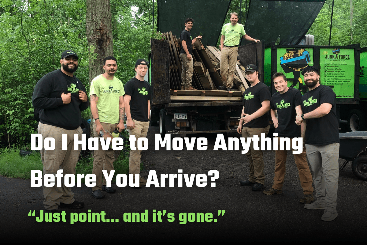 Group of six smiling Ohio Junk Force team members in black shirts and caps pose by green dump truck loaded with pallets in wooded area; text states "Do I Have to Move Anything Before You Arrive? Just point...and it's gone."