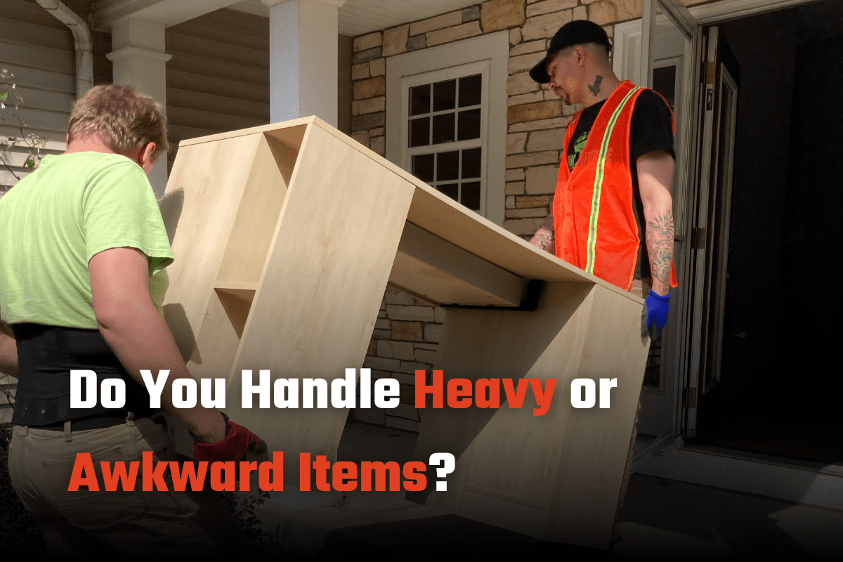 Two Ohio Junk Force workers—one in green shirt and orange safety vest—carry a large awkward wooden cabinet through brick house doorway; red and black text asks "Do You Handle Heavy or Awkward Items?"