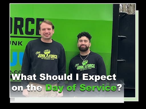 Two friendly Ohio Junk Force crew members in branded black sweatshirts stand smiling in front of green company truck; green text overlay reads "What Should I Expect on the Day of Service?" previewing junk removal process.