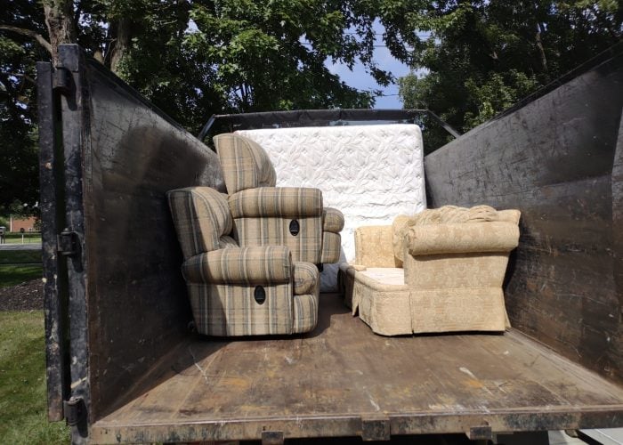 Usable unwanted furniture, including recliners, an upholstered chair, and a mattress, loaded neatly inside a junk removal truck for donation or disposal.