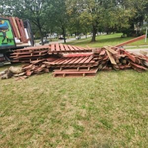 Large pile of broken wooden pallets and scrap lumber stacked on a grassy area next to an Ohio Junk Force truck during a junk removal job.