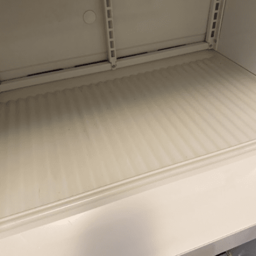 A close-up view of a clean, empty ridged shelf inside a white refrigerator.