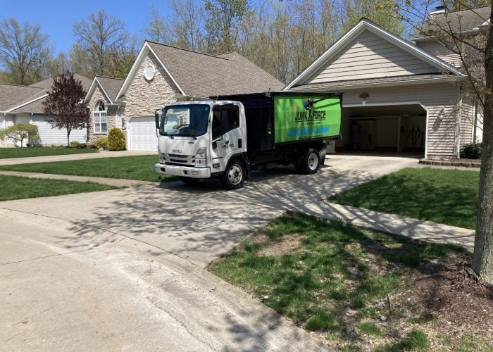 A white and green Ohio Junk Force truck parked in a residential driveway on a bright, sunny day.